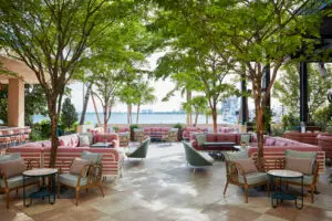 Outside Terrace featuring pink cushioned sofas, teal tile bar stools, and lush greenery overlooking the bay.