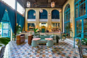 Elegant Casadonna bar lounge with high ceilings, teal drapes, marble floors, and plush seating around pink tables, framed by arched windows and vintage chandeliers.