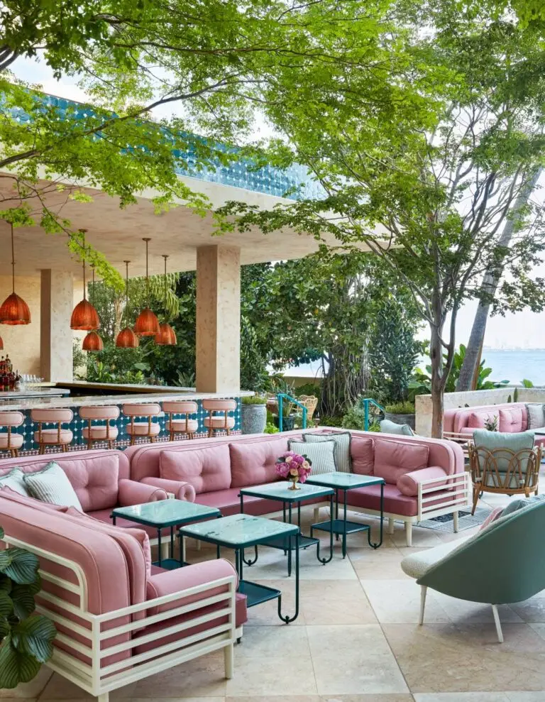 Outdoor lounge at Casadonna Miami featuring pink cushioned sofas, teal tile bar stools, and lush greenery overlooking the bay.